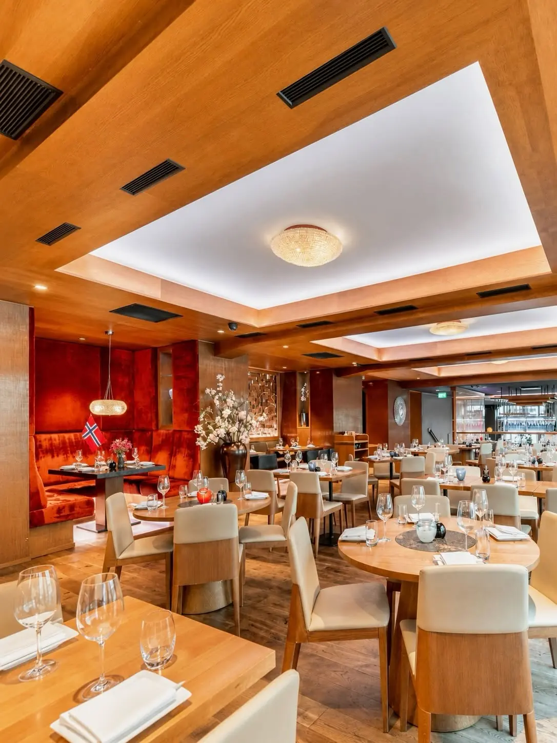 NAMA's dining room in daylight with oak tables, red velvet booth and set glassware