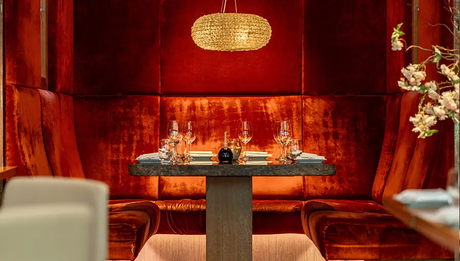 Private red velvet booth set for dinner under a woven pendant light