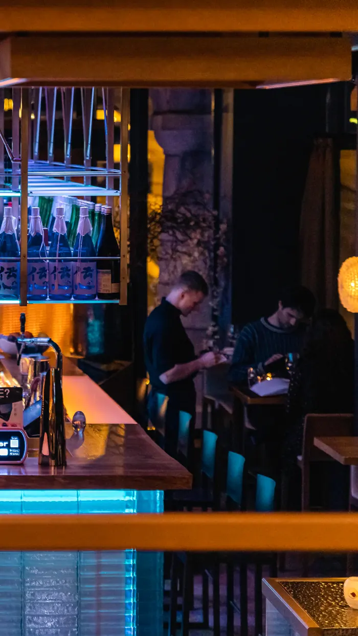 Evening at the bar counter with sake bottles and guests dining behind