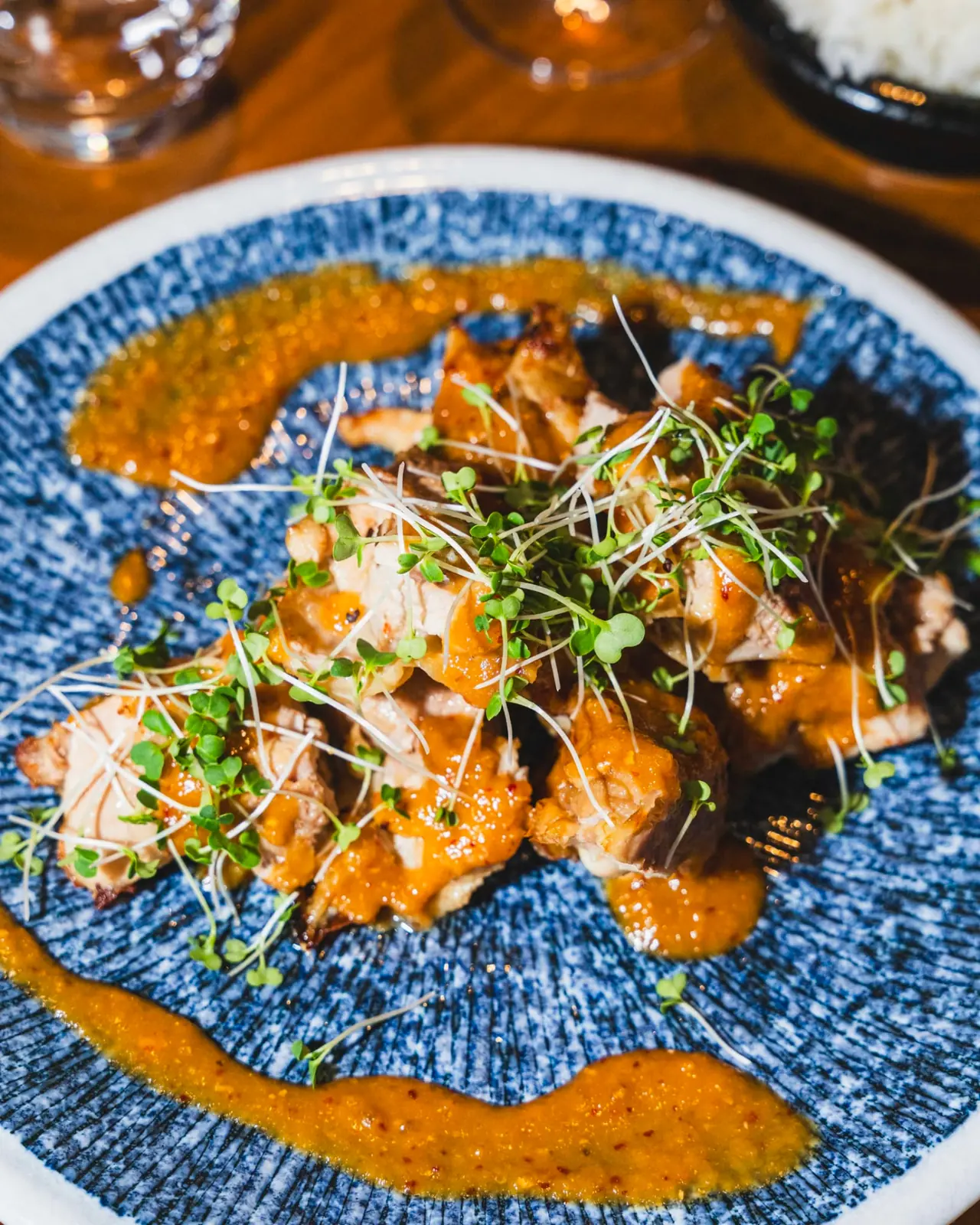 Robata-grilled chicken with sprouts and spiced sauce on a blue ceramic plate