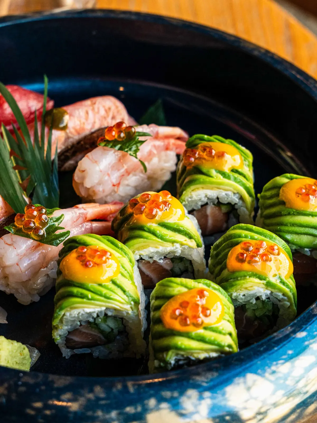 Avocado-wrapped maki and nigiri with roe in a dark ceramic bowl