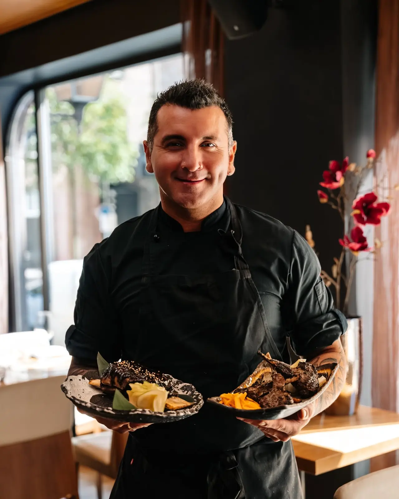 NAMA chef holding two plates of grilled dishes in the dining room
