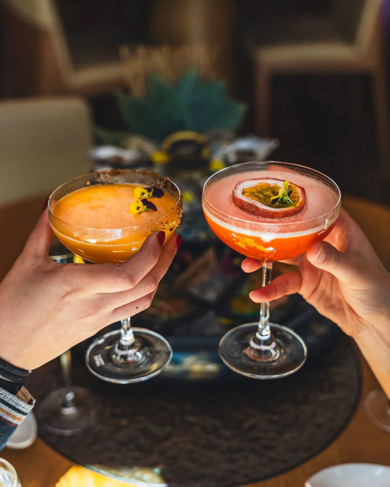 Two guests toasting with citrus cocktails garnished with edible flowers and passion fruit