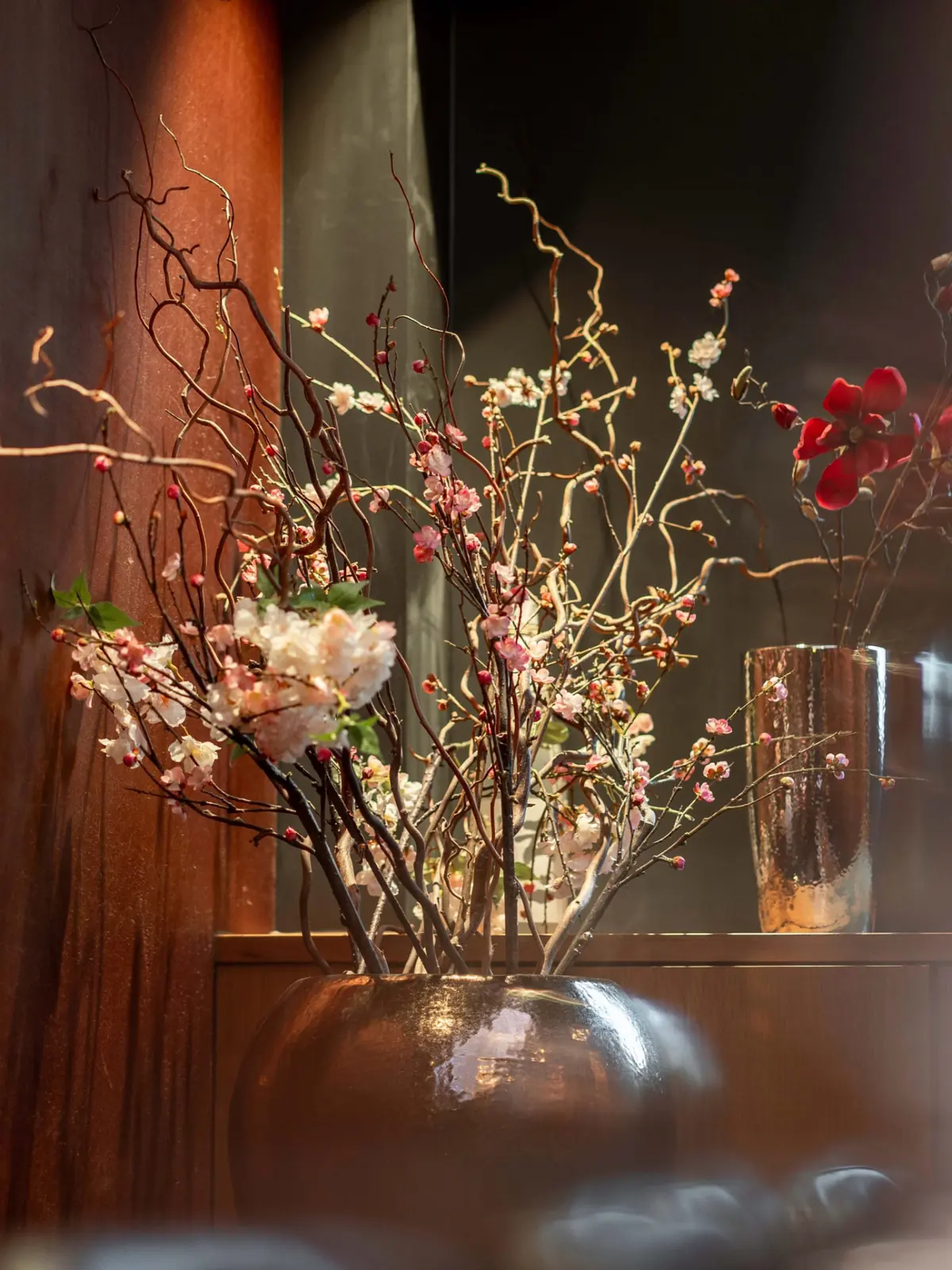 Blossom branches in a bronze vase against warm wood in the dining room