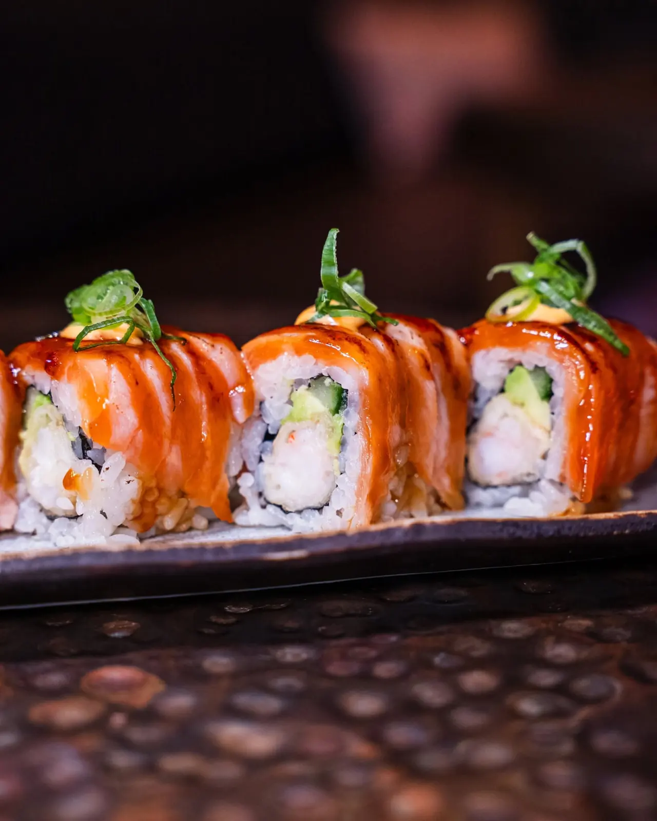 Torched salmon roll with avocado and spicy mayonnaise on a dark ceramic plate